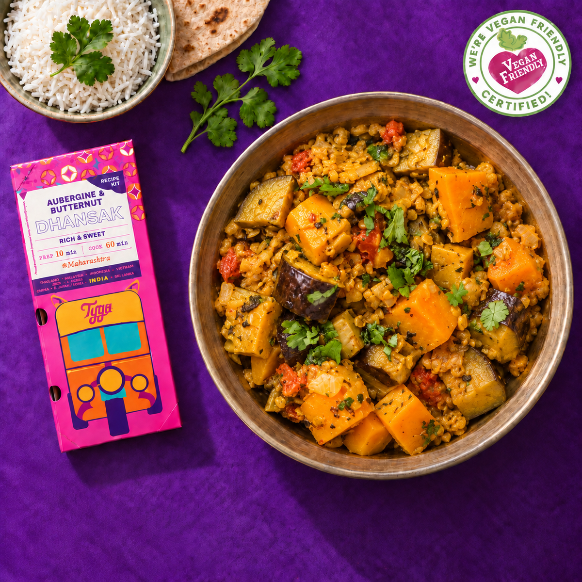 Aubergine and butternut squash Dhansak in a brass bowl beside the colourful Tyga recipe kit